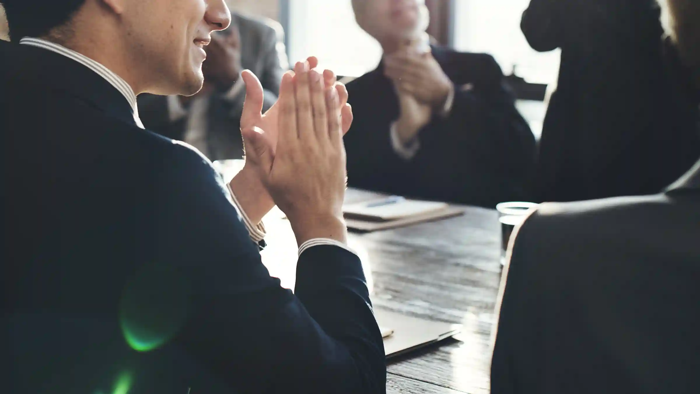 workshop-fuehrungskraefte-austausch-sponsorship-desktop Mann in Anzug mit gefalteten Händen während einer Besprechung in einem Konferenzraum.